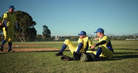 Baseball teammates relaxing on outfield grass in yellow uniforms, teamwork and camaraderie