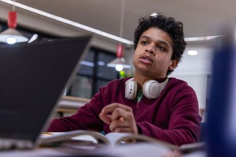 African american teen studying and focusing with laptop and headphones in modern library