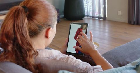 Woman using tablet on sofa shopping for clothes at home, tapping touchscreen