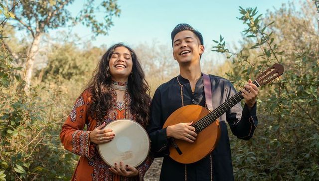 Sunlit boho music duo singing and playing mandolin with frame drum on woodland trail