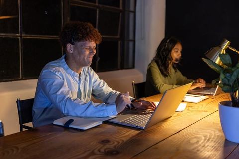 African american coworkers collaborating late with headsets on laptops in modern office