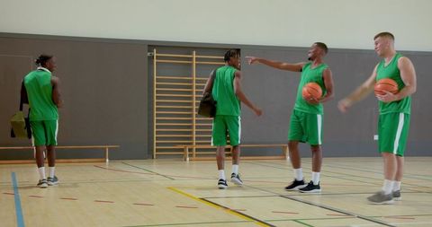 Diverse male basketball team entering gym warming up for scrimmage with dribbling and passing drills