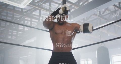 Backlit shirtless boxer wiping sweat with glove in ring training high-contrast rimlight