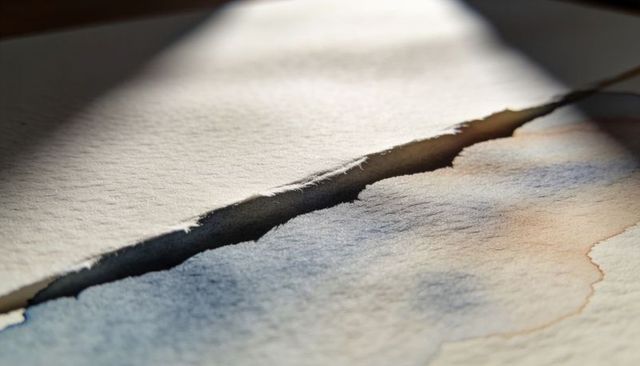 Deckled tear on cold-press watercolor paper revealing granular washes and fiber texture