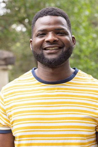 Smiling man wearing yellow striped t-shirt outdoors with soft bokeh green background