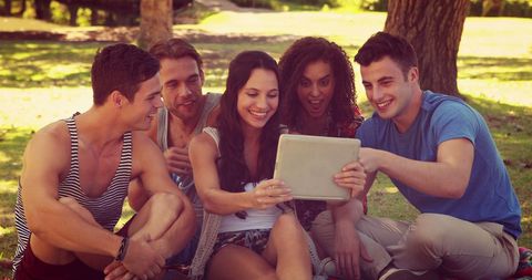 Diverse Young Adults Sharing Fun Experience on Tablet in Park