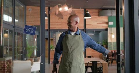 Cafe owner opening door and welcoming customers with warm smile in modern wood interior