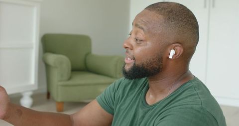 African american man smiling and listening with wireless earbud after workout at home