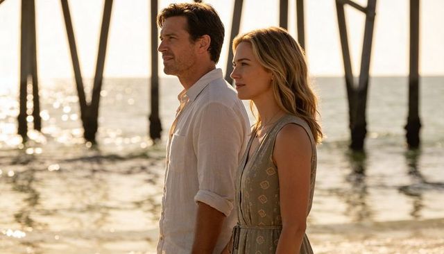 Couple gazing toward horizon on sunlit beach by pier pillars at golden hour