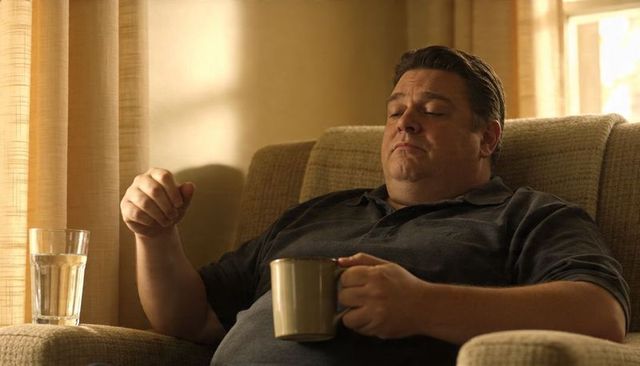 Middle-aged man relaxing on recliner holding mug in sunlit living room