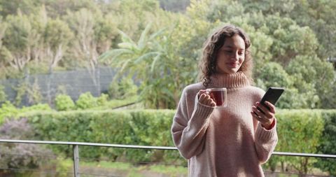 Woman Enjoying Coffee While Browsing Smartphone on Balcony in Nature