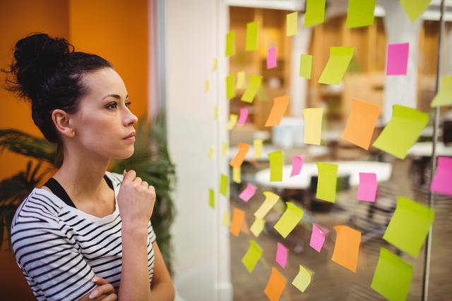 Female executive intensely focusing on colorful sticky notes in an office environment. Ideal for visuals related to business strategy sessions, creativity, planning and organization concepts, productivity articles, and workplace dynamics.