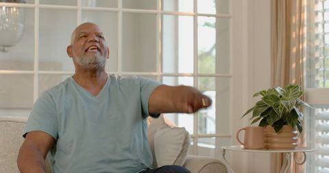 Senior man watching tv at home, showing emotion in living room
