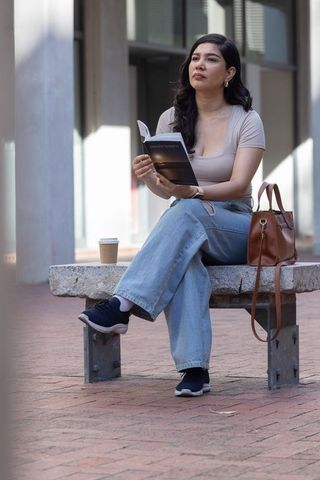 Urban reader enjoying coffee and paperback on sunlit stone bench in plaza