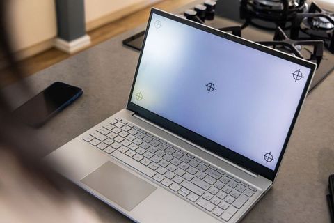 Silver laptop open on kitchen countertop displaying screen markers with smartphone nearby