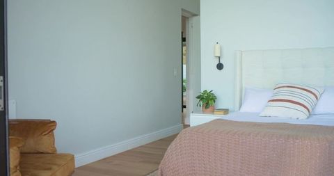 Serene minimalist bedroom featuring dusty-rose knit throw, neutral headboard and greenery
