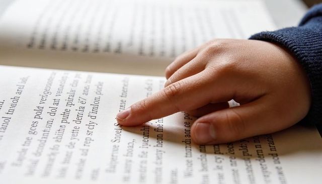 Child tracing text with finger on open book, early literacy learning and focus close-up
