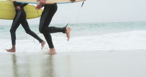 Low Section of Surfers Running at Beach with Surfboards on Overcast Day