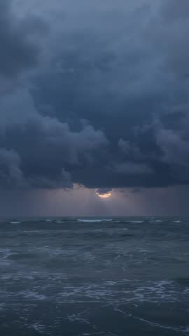 Moody storm clouds parting, sun peeking through over restless ocean waves vertical video
