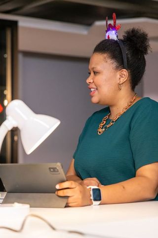 African american woman wearing light-up antler headband working on tablet at modern desk