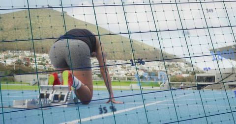 Sprinter preparing for explosive start on blue track with analytics data grid overlay