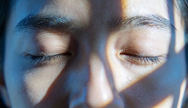 Resting face receiving striped light and shadow showing closed eyes and textured skin