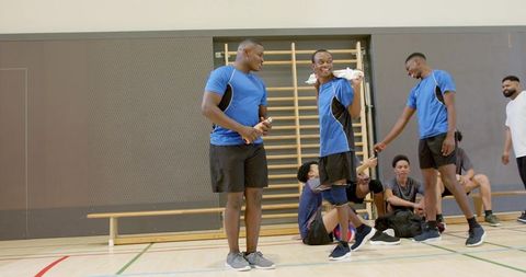 Diverse male teammates chatting and warming up at wall bars during indoor sports practice