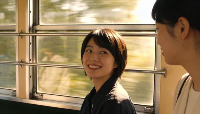Smiling asian woman chatting on moving train bench with sunlight and motion blur