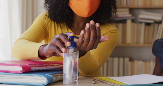 African American woman disinfecting hands with sanitizer near bookshelves - Download Free Stock Images Pikwizard.com