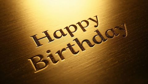 Shining embossed happy birthday lettering on brushed gold plate evoking luxury celebration