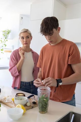 Teen preparing green smoothie while woman watching in bright minimalist kitchen