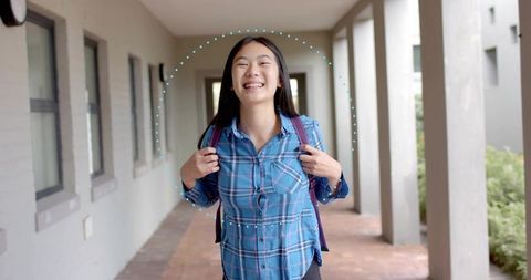 Smiling Asian student walking school corridor carrying purple backpack wearing plaid shirt