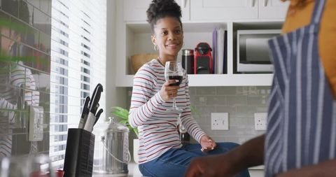 Young woman sitting on countertop holding red wine glass smiling in modern kitchen