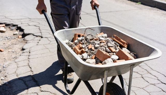 Construction worker pushing wheelbarrow with bricks, rubble and rebar on cracked road