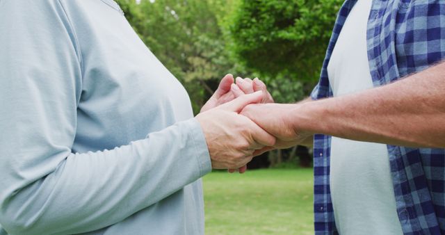 Senior couple holding hands in a park shows love and togetherness in nature. Ideal for themes related to elderly relationships, emotional support, outdoor activities, and peaceful moments.