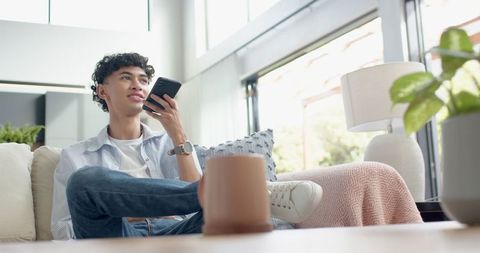 Asian Man Relaxing with Smartphone in Modern Living Room