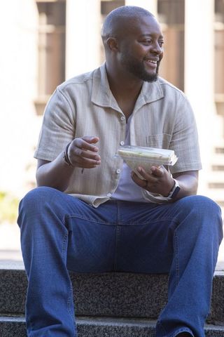African man enjoying takeaway lunch on stone steps smiling casual urban lifestyle