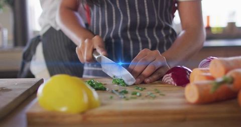 Teenager chopping fresh herbs and vegetables on wooden cutting board in home kitchen