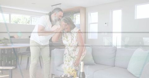 Couple celebrating surprise birthday at home with cake and champagne in modern living room