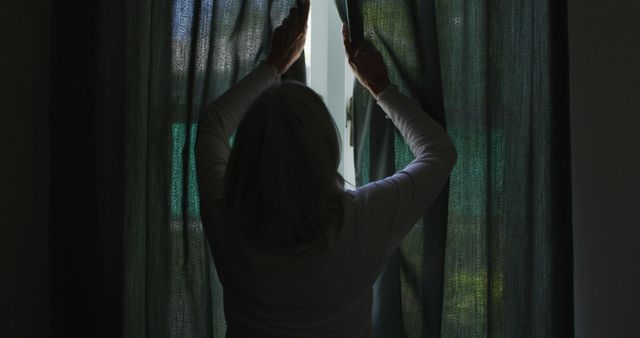 Caucasian senior woman standing by window and closing curtains. Relaxation, wellbeing, retirement and senior lifestyle.
