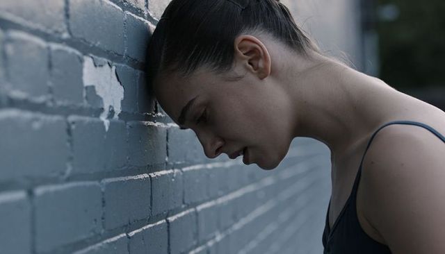 Young woman leaning forehead on painted brick wall moody desaturated urban portrait