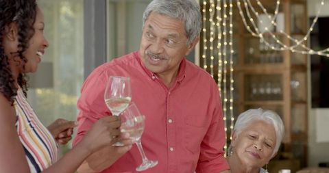 Senior couple raising wine glasses with African American woman celebrating family toast