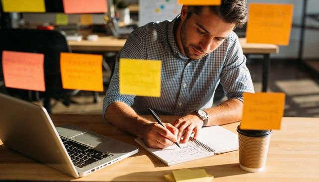 Focused designer planning workflow with sticky notes and laptop in coworking space
