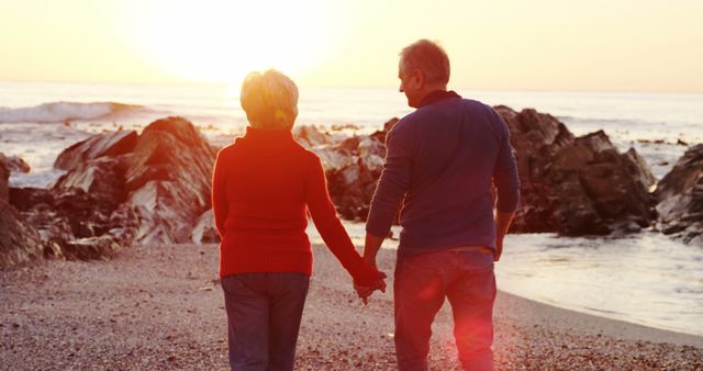 Senior caucasian couple holding hands and walking on beach by sea at sunset. Retirement, relationship, love, togetherness, free time and relaxing, unaltered.