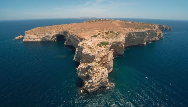 Aerial view of rugged flat-topped headland with sea caves and layered limestone cliffs