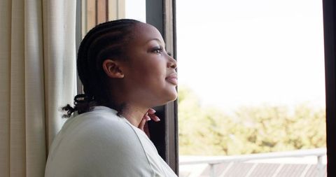 African American woman leaning at open window gazing outward, contemplative morning light