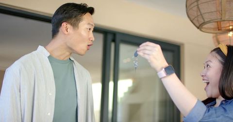 Asian couple celebrating new home with keys at doorway modern apartment surprise reaction