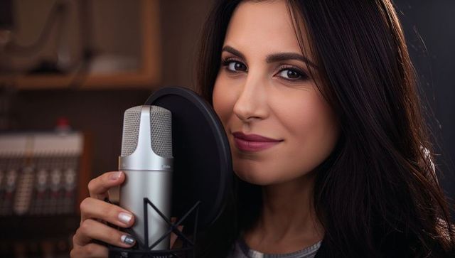 Confident female vocalist recording with condenser microphone and pop filter in studio