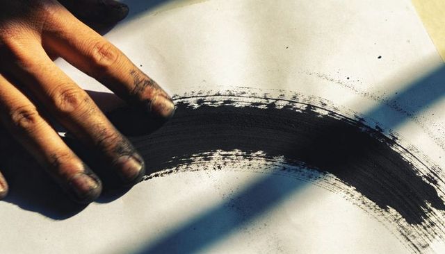 Creating bold black ink arc with stained fingers on white paper, shadow interplay