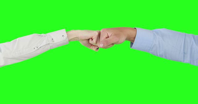 Two individuals are engaging in a fist bump, one wearing a white sleeve and the other in a blue sleeve, against a green screen background, with copy space. This gesture often signifies agreement, camaraderie, or a casual greeting between people.